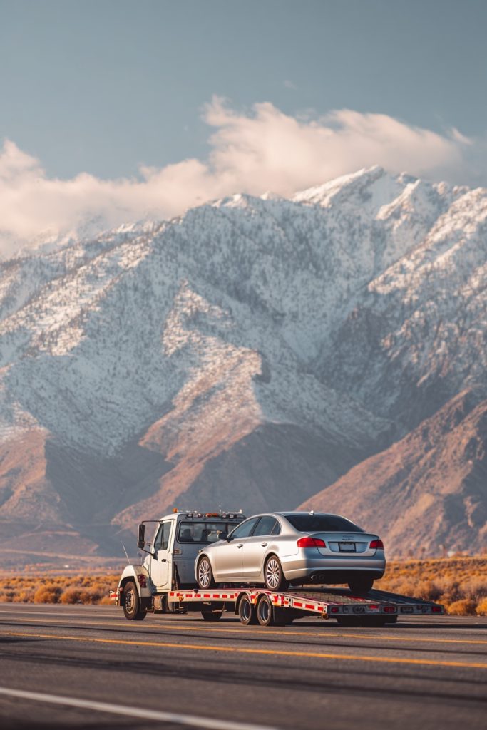 Local & Long-Distance Towing by Tow Truck Now with a sedan on a flatbed truck along a mountain highway